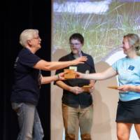Teacher receives plaque from Groundswell staff in front of projected "Groundswell" background
